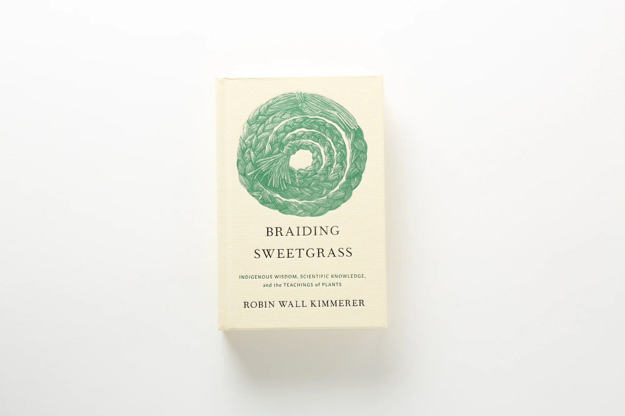 A photograph of the book "Braiding Sweetgrass", by Robin Wall Kimmerer. The cover bears an illustration of a coiled braid of sweetgrass.