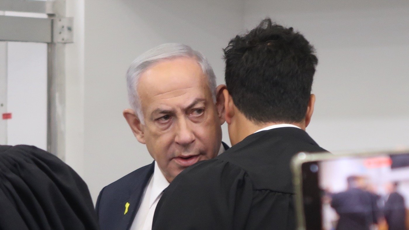 Benjamin Netanyahu in court during his corruption trial, talking with his attorney Amit Hadad (from Wikipedia; photo by Oren Persico, The Seventh Eye)